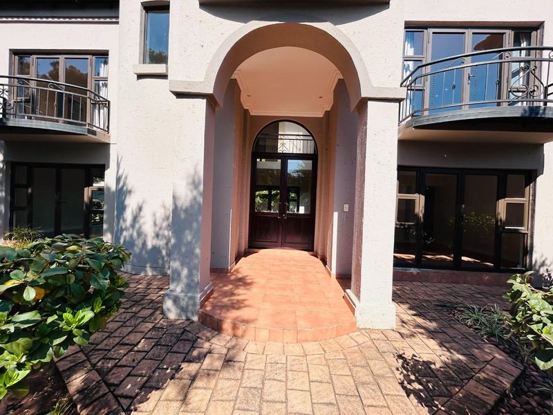 Front entrance featuring an arched portico, tiled porch, and double glass doors, flanked by upper-level balconies with wrought iron railings.