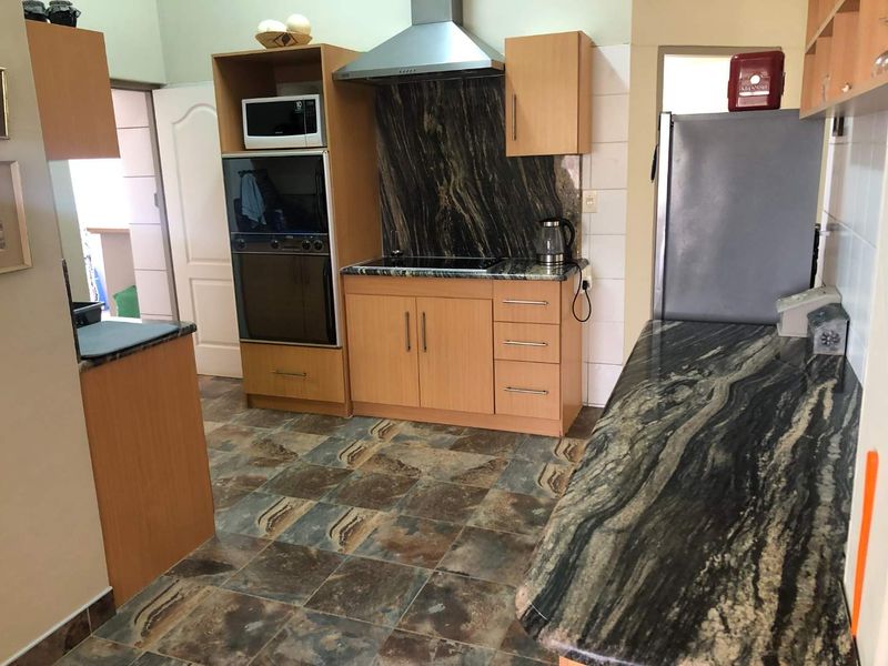 Functional kitchen featuring wood-veneer cabinetry, dark granite countertops, built-in oven, and stainless steel extractor fan with tiled splashback.