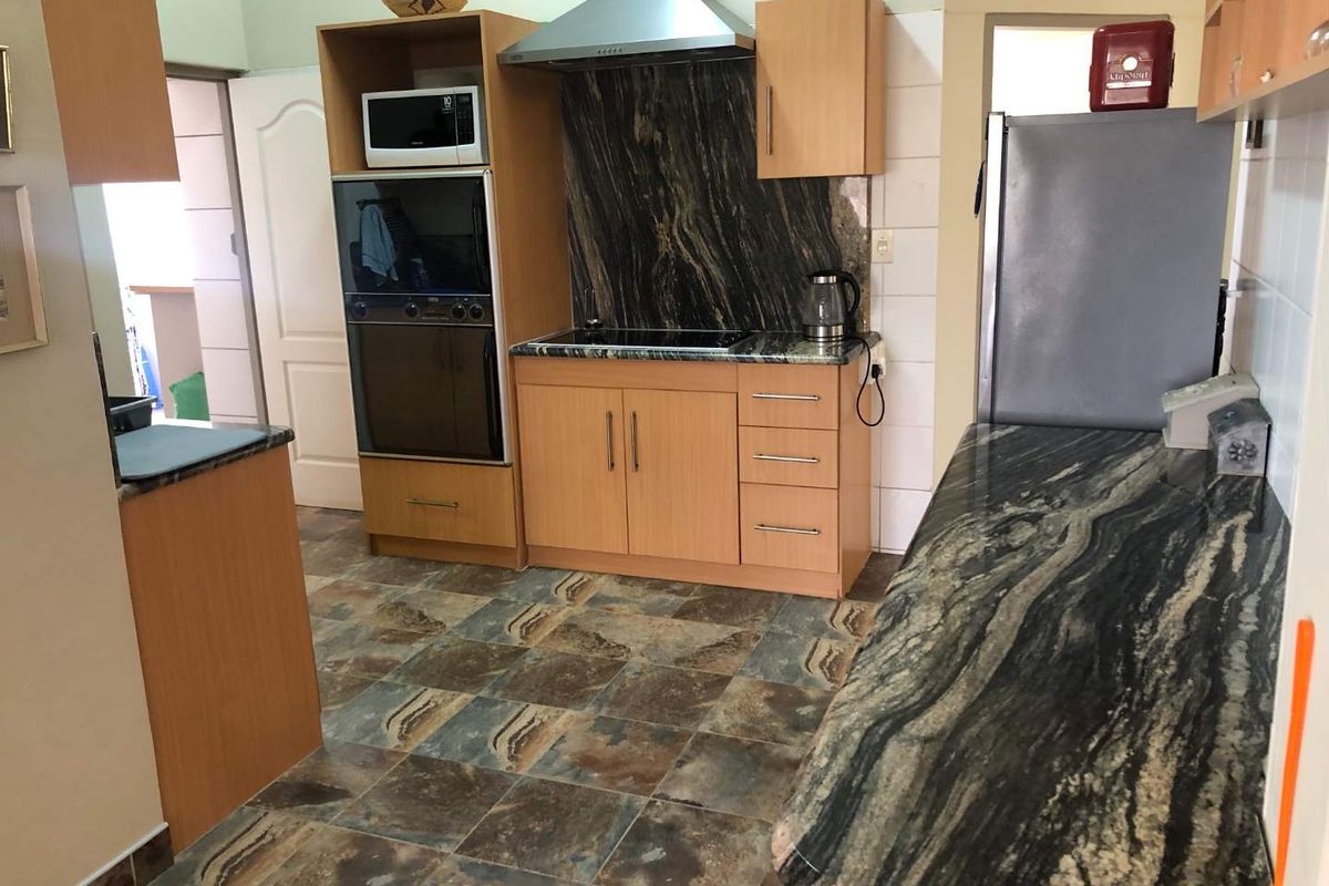 Functional kitchen featuring wood-veneer cabinetry, dark granite countertops, built-in oven, and stainless steel extractor fan with tiled splashback.