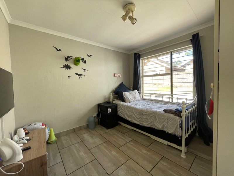 A functional bedroom featuring tiled flooring, a window with security bars, and a ceiling-mounted light fixture.
