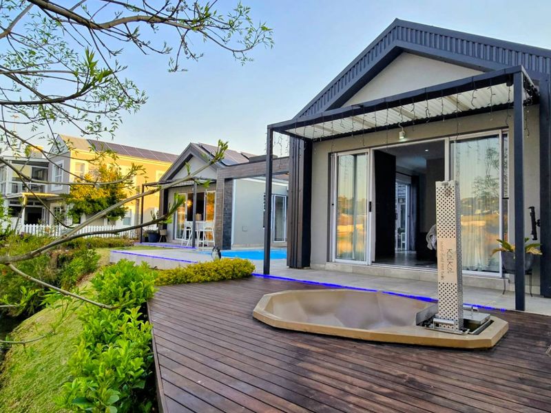 Modern waterfront residence featuring timber decking, a sunken fire pit, and a swimming pool with seamless indoor-outdoor flow through sliding glass doors.