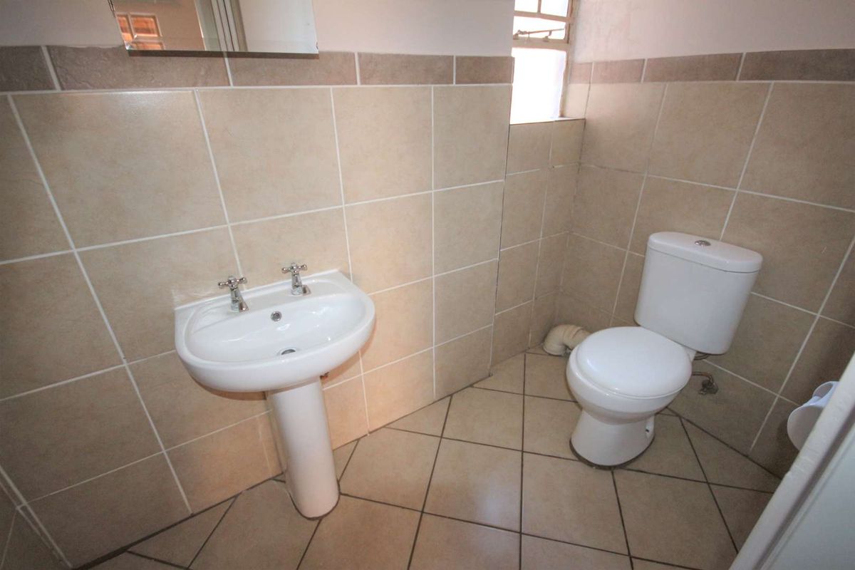 A functional bathroom featuring a pedestal basin and a standard toilet, finished with neutral wall and floor tiling.