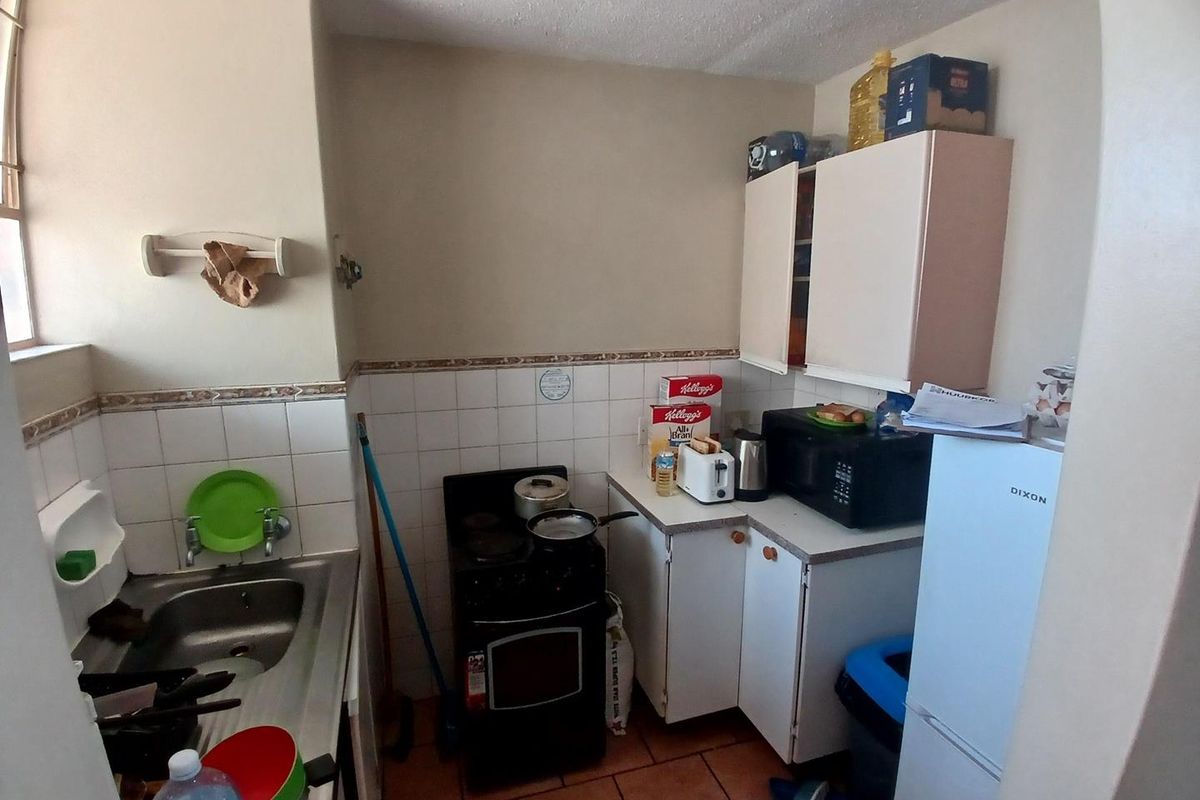 Compact kitchen featuring tiled flooring, a stainless steel sink, built-in cabinetry, and a tiled backsplash, offering a functional layout for renovation.