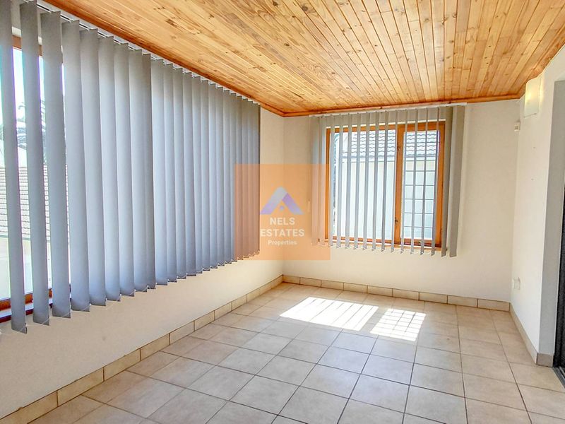 A bright, enclosed patio or sunroom featuring a timber-clad ceiling, tiled flooring, and large windows with vertical blinds.