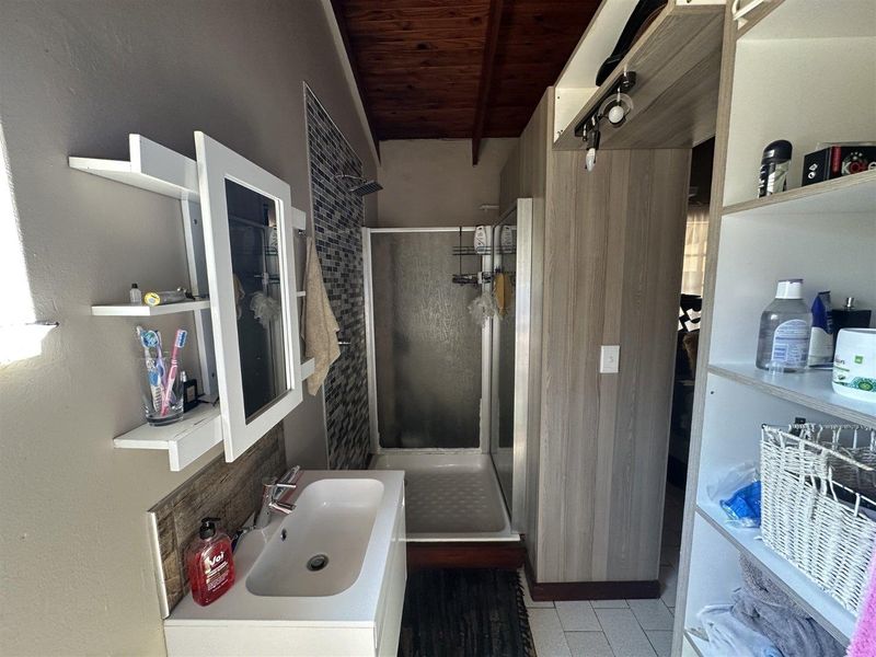 A functional bathroom featuring a shower enclosure, vanity basin with mixer tap, and built-in shelving, complemented by a timber ceiling.