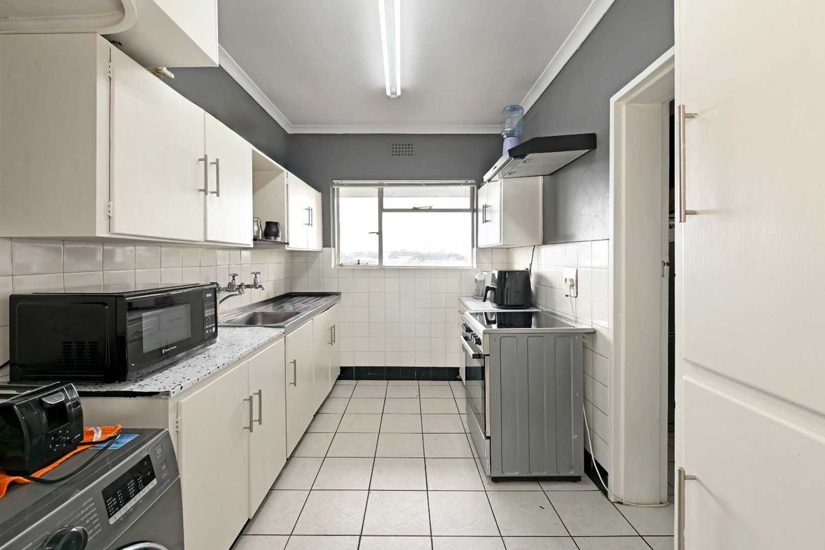 A functional galley-style kitchen featuring white cabinetry, tiled backsplash, tiled flooring, and a stainless steel sink with integrated extractor fan.