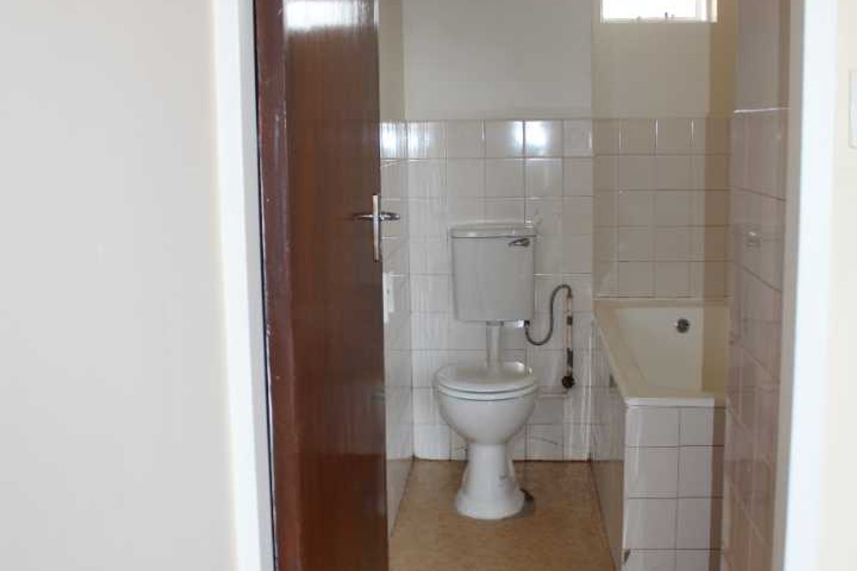 A compact bathroom featuring a standard toilet, bathtub, and wall-mounted electric water heater with tiled wall finishes.