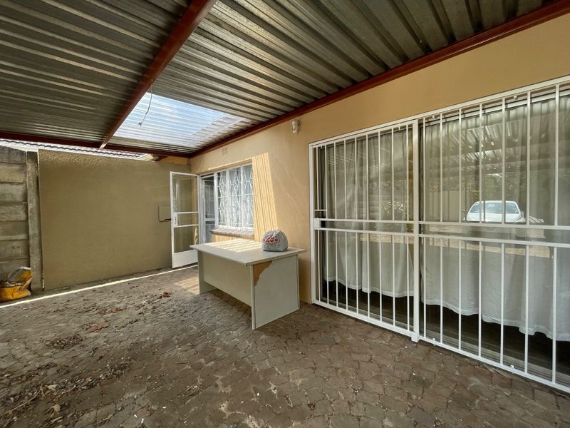 A covered outdoor patio area featuring paved flooring, a corrugated metal roof with a translucent panel, and secure sliding glass doors.