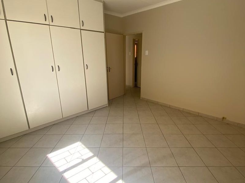 A spacious, empty bedroom featuring neutral tiled flooring, built-in cupboards, and a simple ceiling light fixture, offering a clean canvas for personalization.