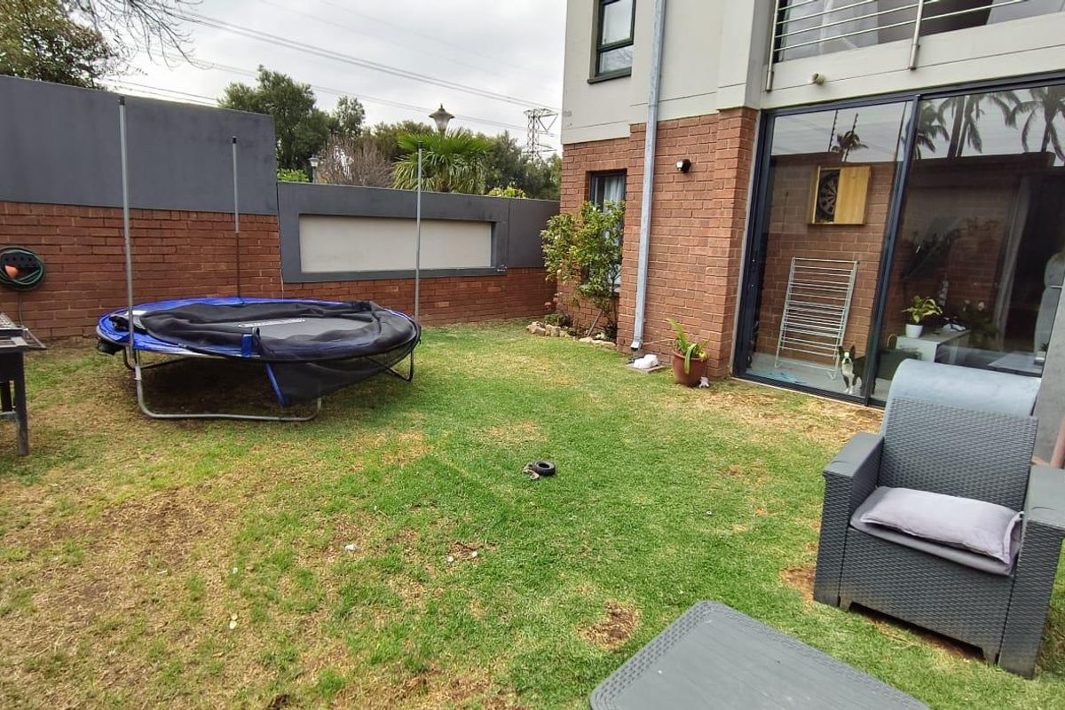 A private rear garden area featuring a brick boundary wall, lawn space, and direct access to the apartment through large sliding glass doors.