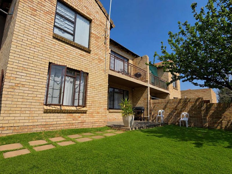 Rear view of a double-story face brick townhouse featuring a private garden, paved patio area, and an upper-level balcony.
