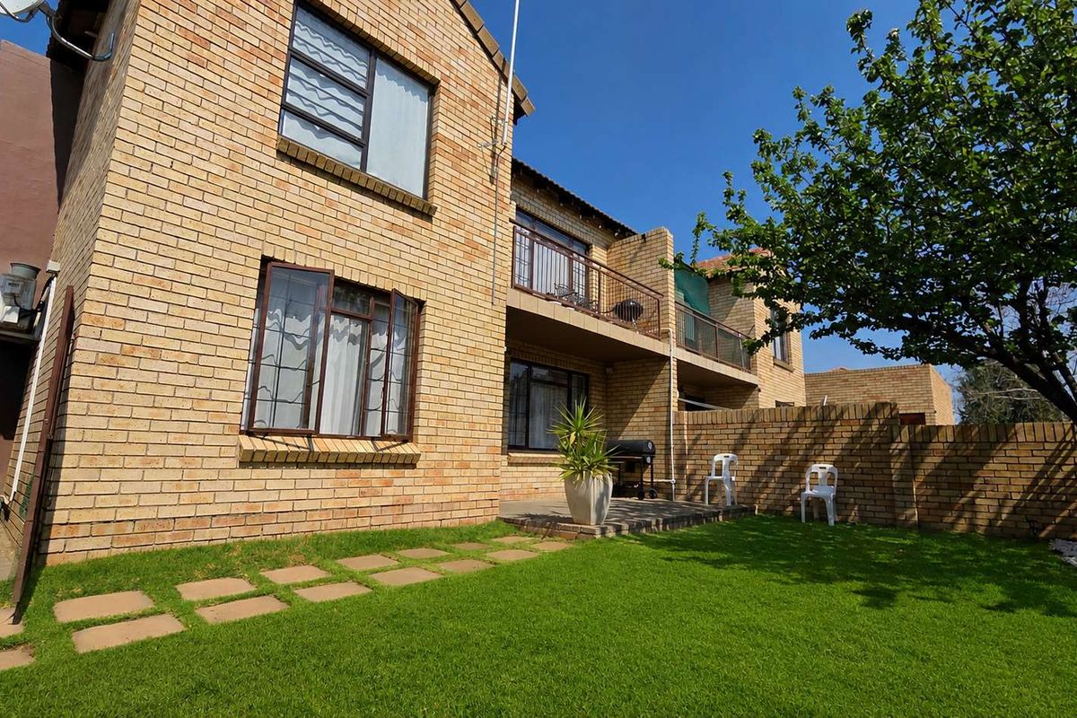 Rear view of a double-story face brick townhouse featuring a private garden, paved patio area, and an upper-level balcony.