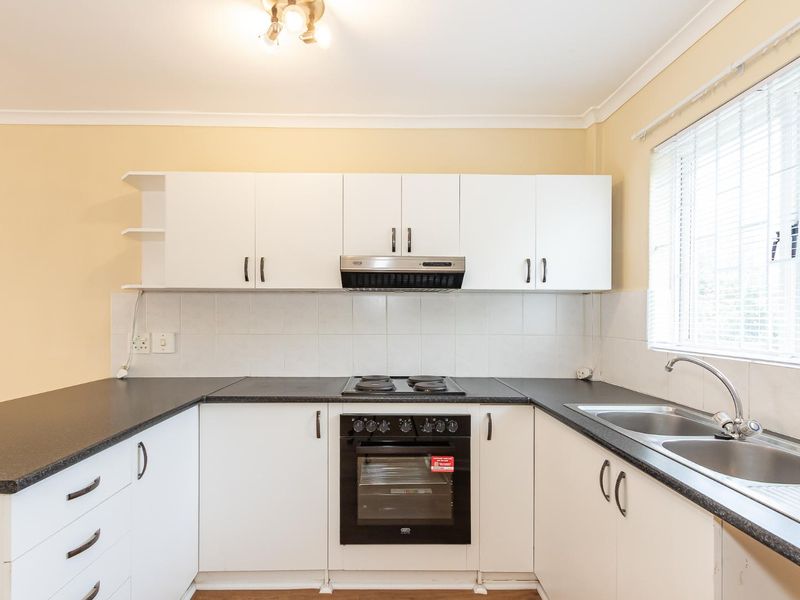 A functional kitchen featuring white cabinetry, dark laminate countertops, a built-in oven with hob, and a double bowl sink with a tiled backsplash.