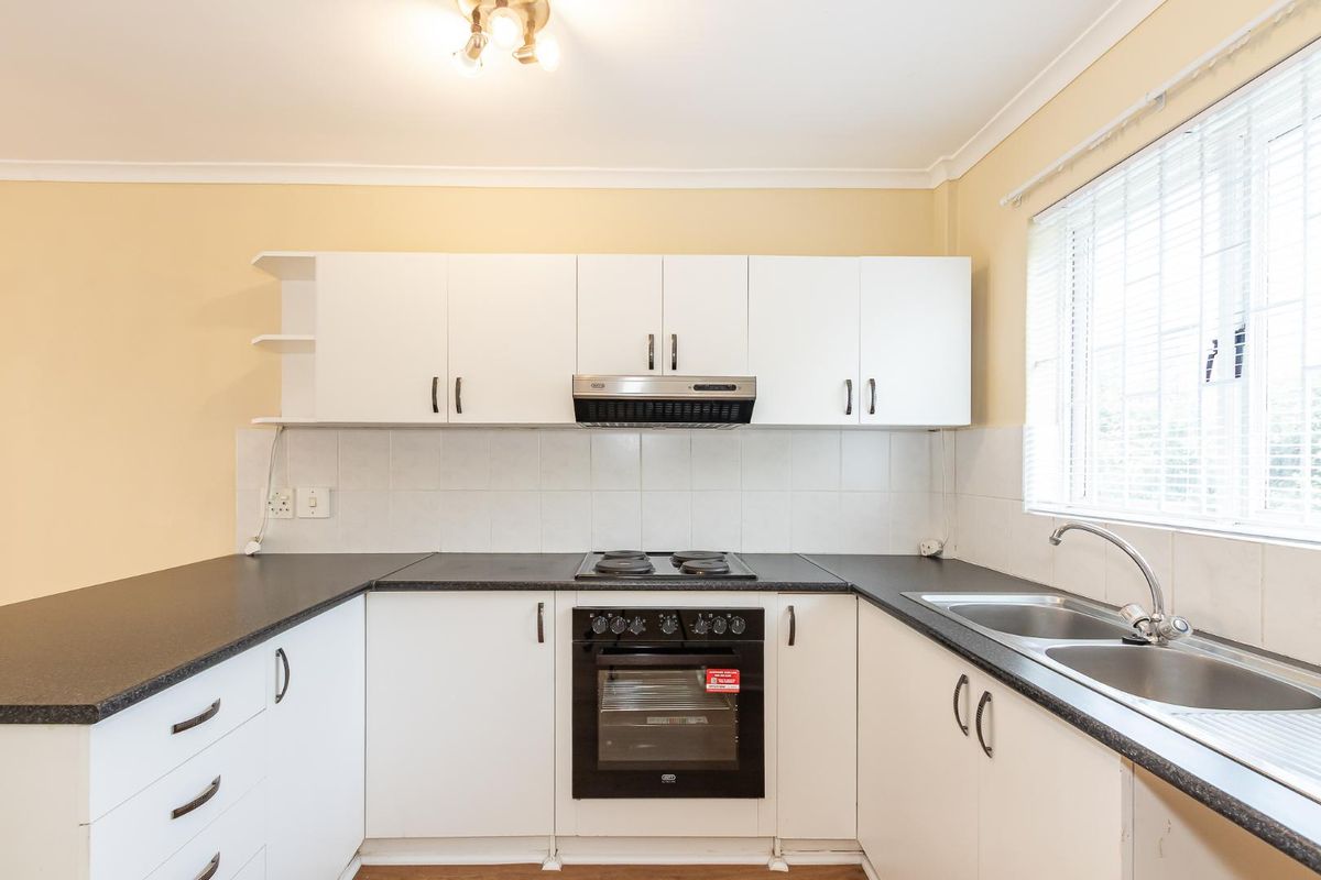 A functional kitchen featuring white cabinetry, dark laminate countertops, a built-in oven with hob, and a double bowl sink with a tiled backsplash.