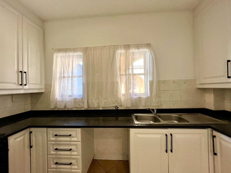 A functional kitchen featuring white cabinetry, black granite countertops, and a double bowl stainless steel sink with tiled backsplash and flooring.