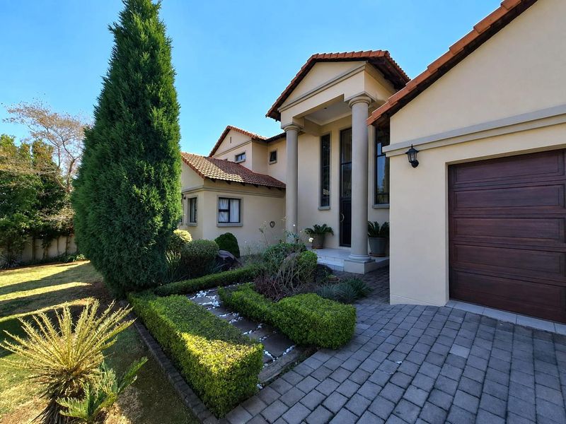 A well-maintained front facade featuring a paved driveway, integrated garage, and classic architectural columns with a landscaped garden entrance.