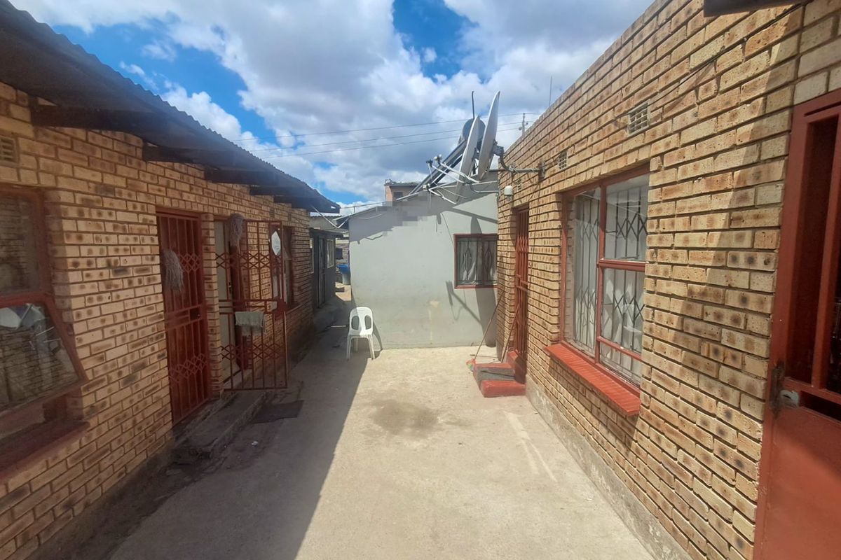 A narrow exterior courtyard area between two face brick structures, featuring concrete paving and security-gated access points.