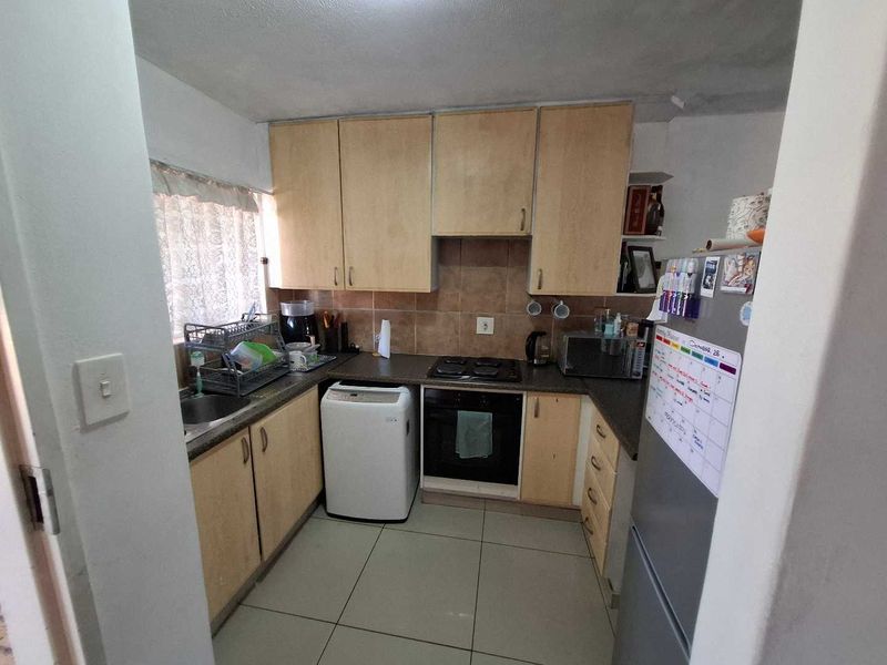 Compact kitchen featuring laminate cabinetry, built-in oven, electric hob, and tiled backsplash, offering a functional layout with potential for modern updates.