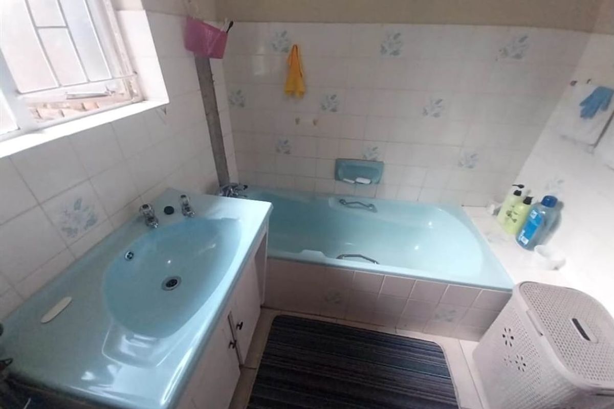A dated bathroom featuring a blue built-in bathtub and matching vanity basin with tiled walls and a window.