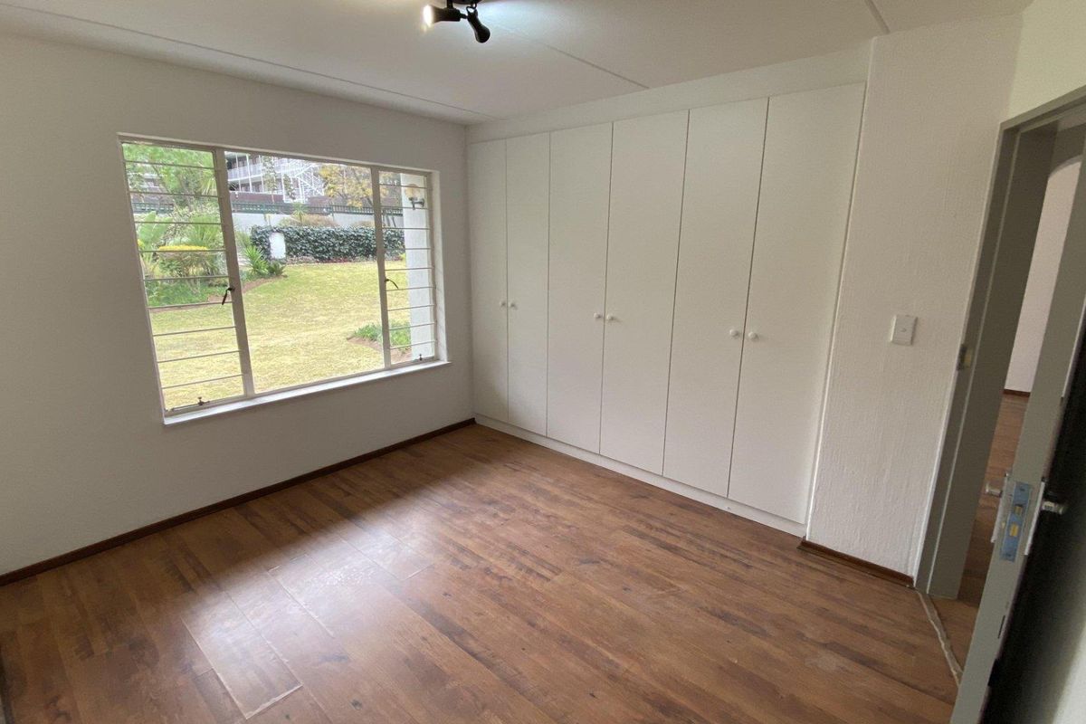 A bright, empty bedroom featuring laminate flooring, large windows with security bars, and extensive built-in cupboard storage.