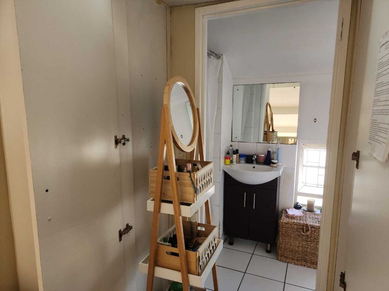 A compact bathroom featuring a vanity cabinet with a basin, tiled flooring, and a window, showing signs of wear and requiring cosmetic updates.