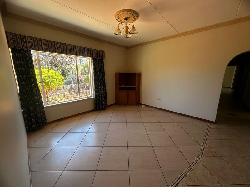 A spacious, empty living room featuring ceramic floor tiles, a decorative ceiling rose, and an arched entryway, offering a blank canvas for interior design.