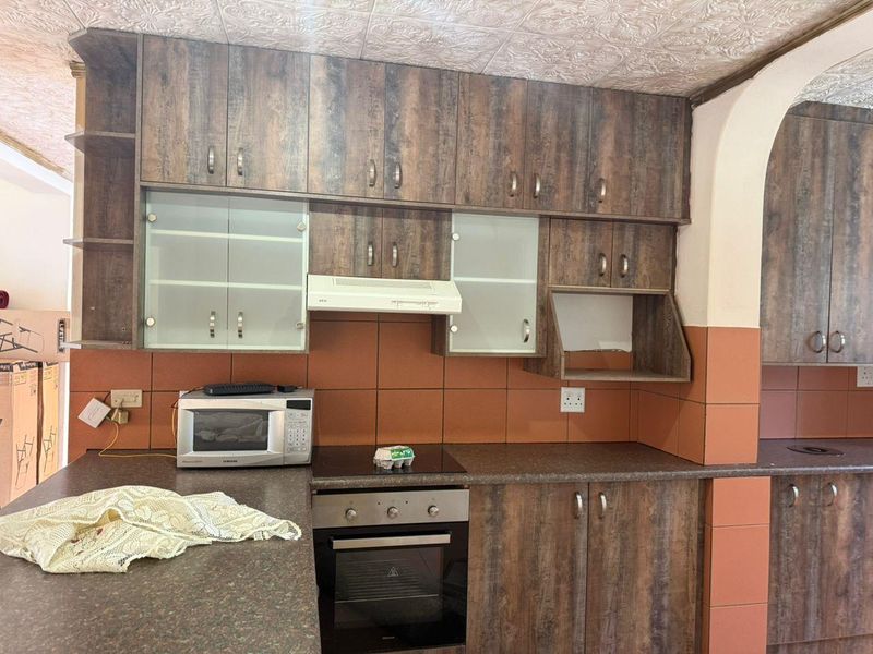 Kitchen featuring wood-look laminate cabinetry, built-in oven, electric hob, extractor fan, and tiled backsplash with textured ceiling finishes.