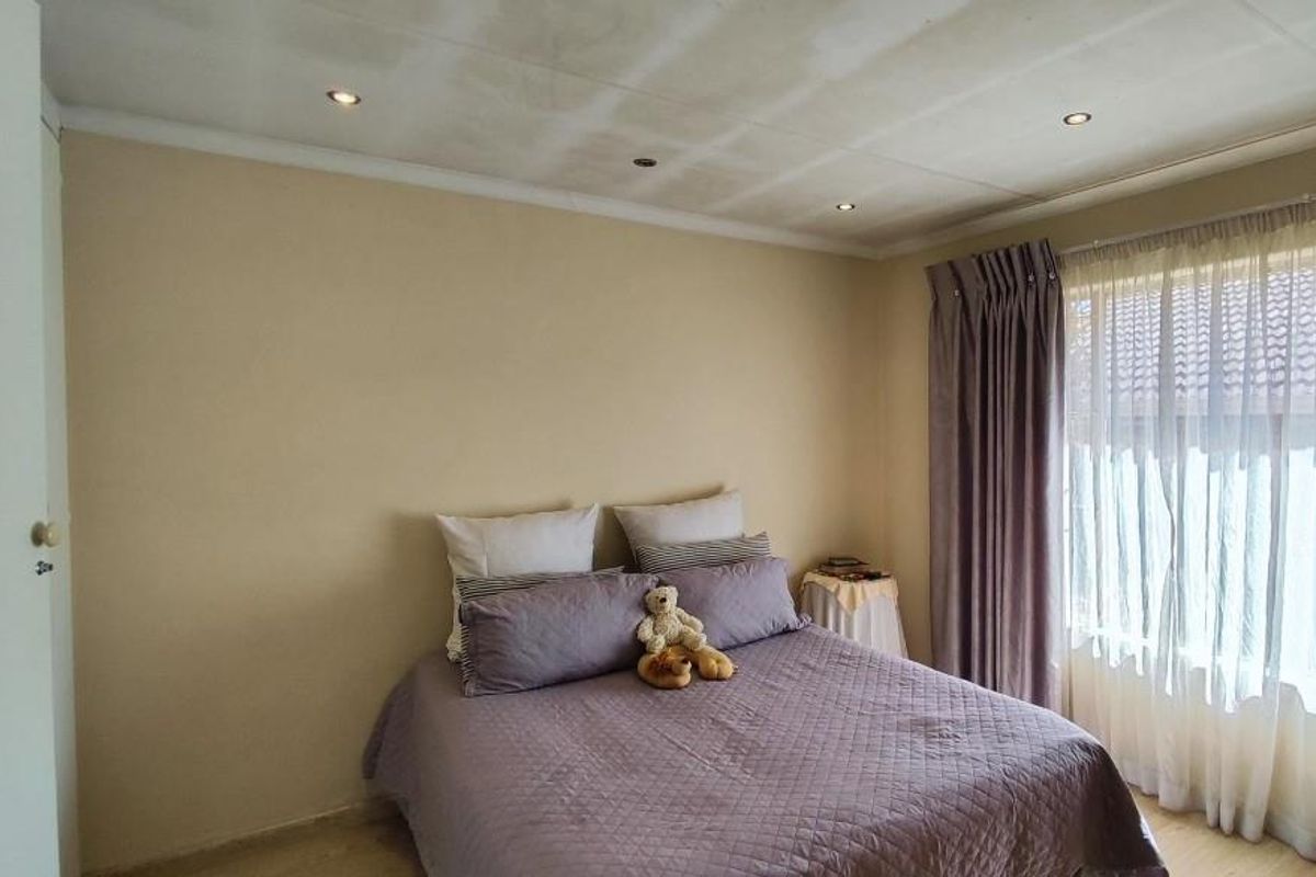 A standard bedroom featuring neutral wall tones, recessed ceiling lighting, and large windows with curtain tracks.