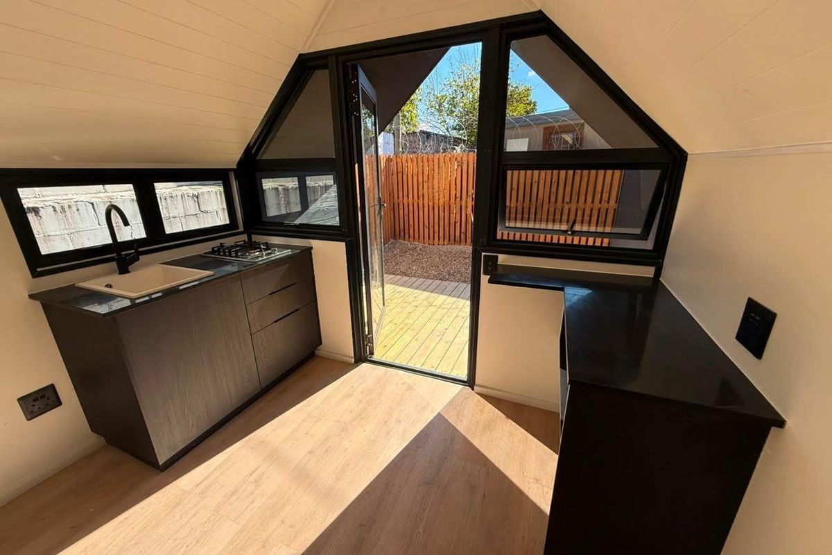 Modern compact kitchen featuring dark cabinetry, stone countertops, gas cooktop, and direct access to an outdoor timber deck.