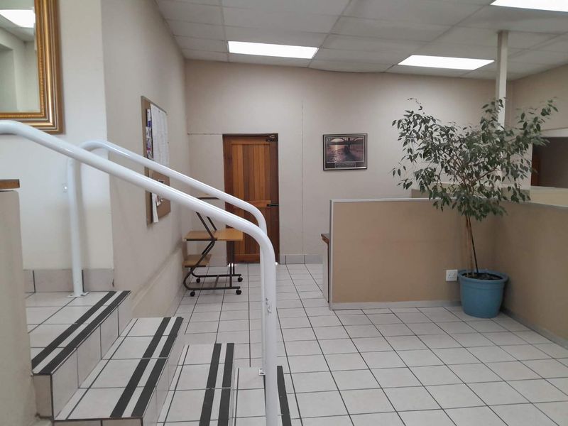Office interior featuring tiled flooring, a staircase with a metal handrail, partition walls, and recessed lighting in a suspended ceiling.