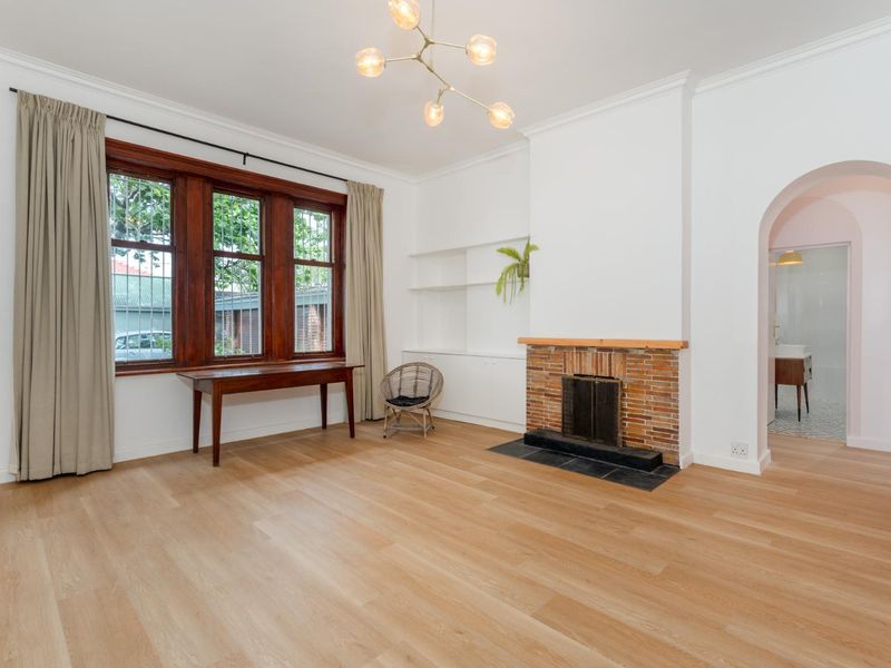 Spacious living room featuring timber flooring, a classic brick fireplace with stone hearth, built-in shelving, and an elegant archway leading to an adjacent room.