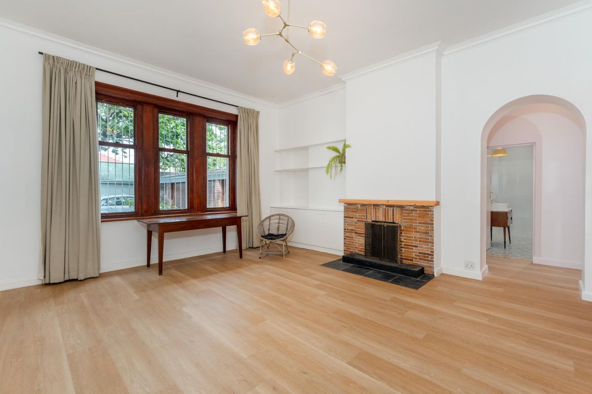 Spacious living room featuring timber flooring, a classic brick fireplace with stone hearth, built-in shelving, and an elegant archway leading to an adjacent room.