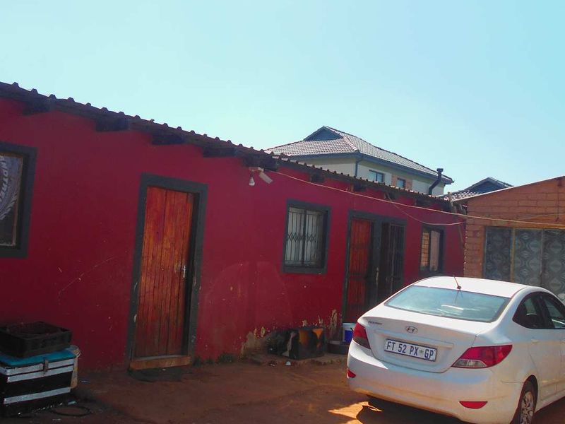 Rear exterior view of the property featuring red painted walls, timber doors with security bars, and exposed roof rafters.