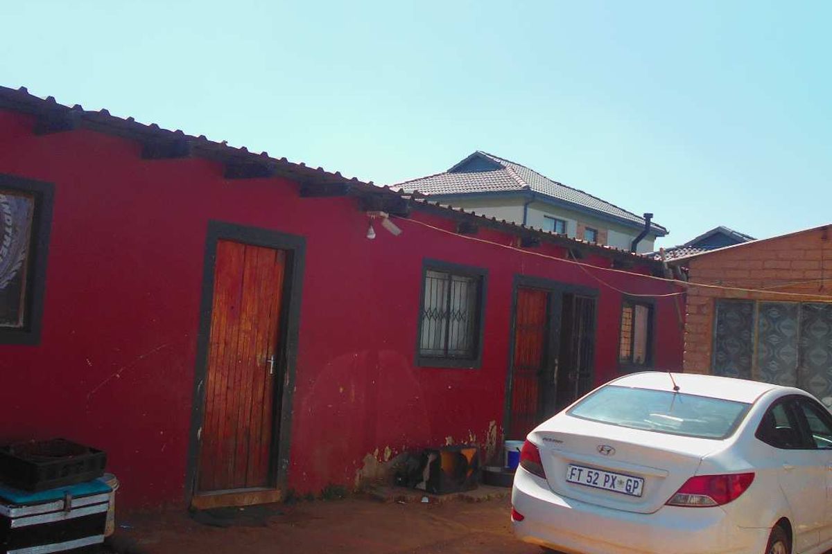 Rear exterior view of the property featuring red painted walls, timber doors with security bars, and exposed roof rafters.