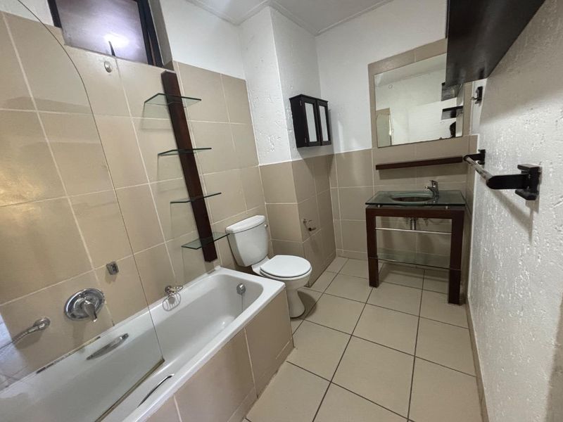 A functional bathroom featuring a bathtub, toilet, and vanity sink with neutral wall and floor tiling.