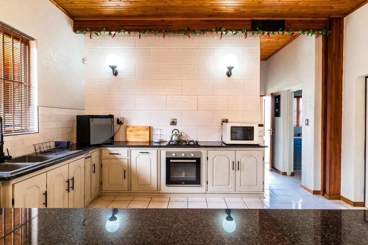 A functional kitchen featuring granite countertops, built-in oven, gas hob, and classic cabinetry under a warm timber-paneled ceiling.
