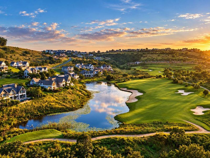 An aerial view of a residential estate overlooking a golf course and a scenic lake at sunset.
