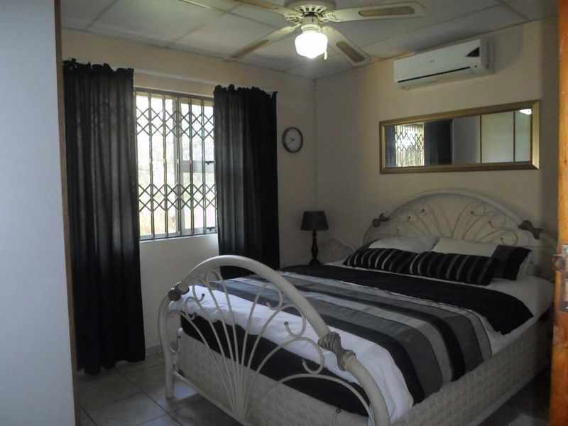 A functional bedroom featuring a ceiling fan, split-system air conditioning, and security bars on the window.