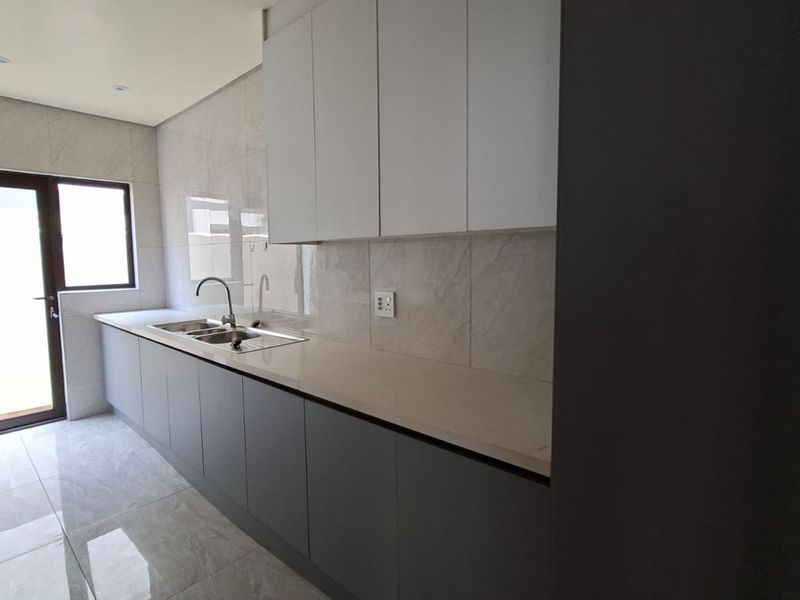 Modern kitchen featuring sleek grey and white cabinetry, stone countertops, stainless steel sink, and polished tiled flooring with direct access to the exterior.