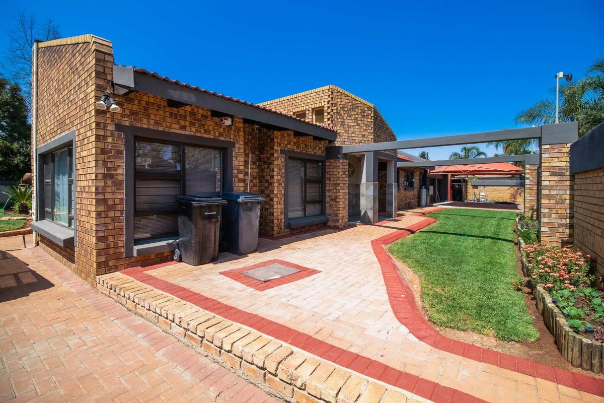 Rear view of the property featuring a face-brick facade, paved patio area, manicured lawn, and a covered outdoor structure.