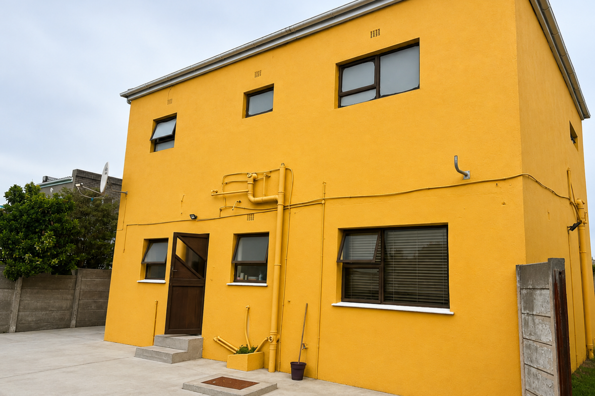 Rear view of a two-story house featuring a bright yellow exterior finish, aluminium window frames, and a concrete paved yard area.