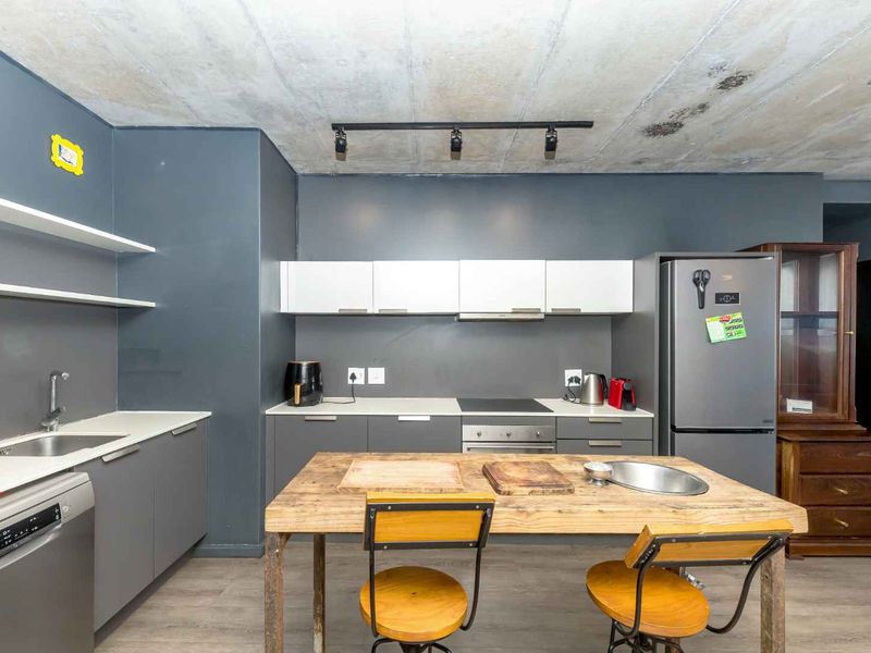 Modern kitchen featuring dark grey cabinetry, exposed concrete ceiling, integrated appliances, and floating shelving, offering a contemporary industrial aesthetic.