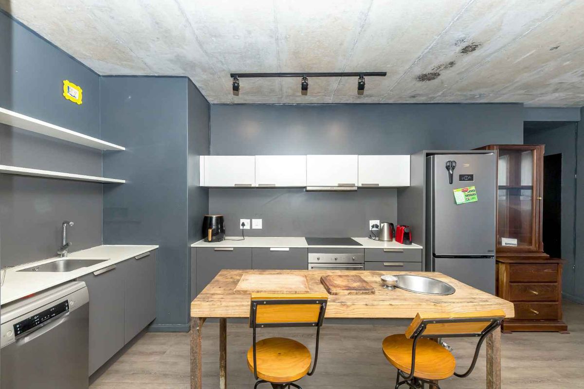 Modern kitchen featuring dark grey cabinetry, exposed concrete ceiling, integrated appliances, and floating shelving, offering a contemporary industrial aesthetic.