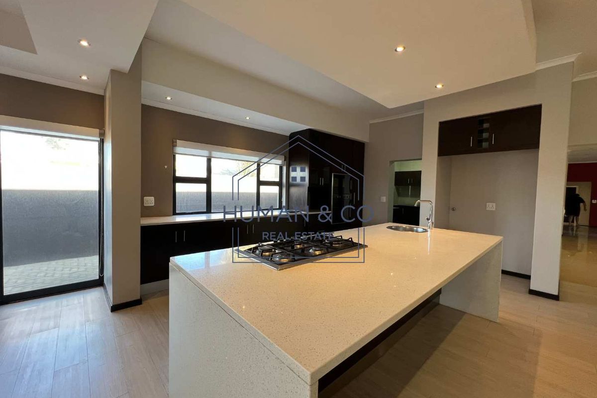 Modern kitchen featuring a large central island with a built-in gas hob, stone countertops, and dark cabinetry with recessed ceiling lighting.