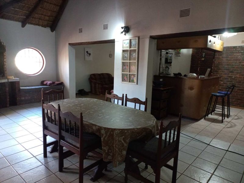 Open-plan living and dining area featuring a thatched roof, exposed beams, a built-in bar, and a distinctive circular window.