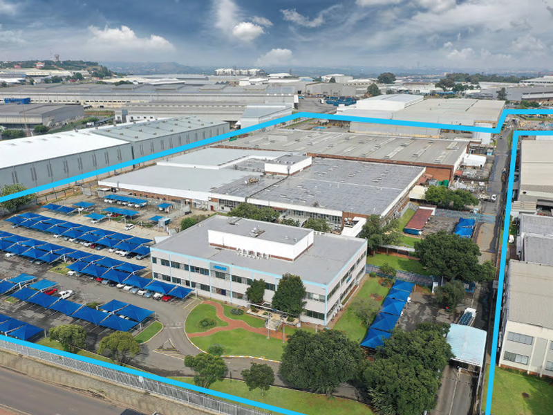 Aerial view of a large industrial facility featuring a multi-story office building, expansive warehouse structures, and extensive paved parking areas with shade ports.