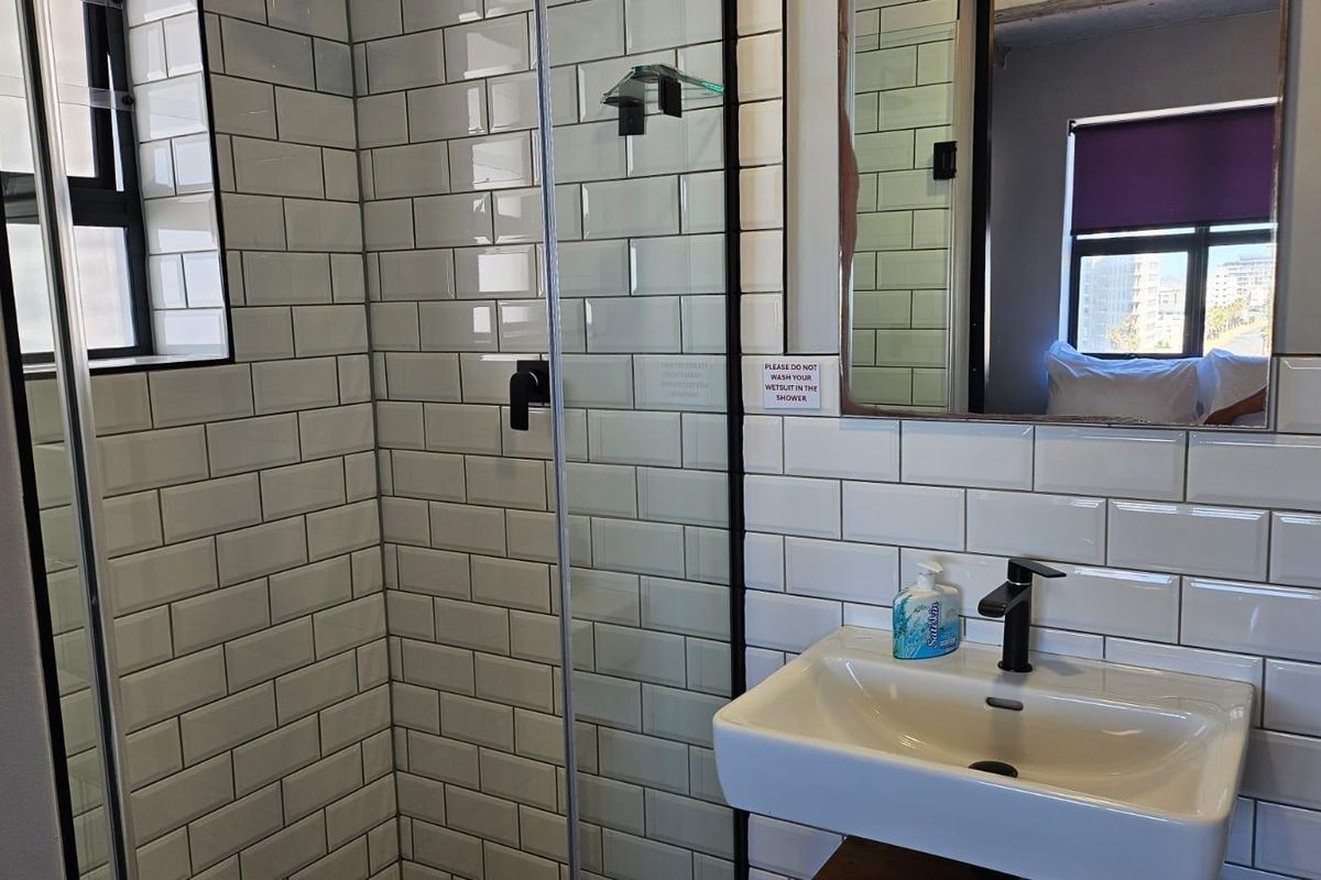 Modern bathroom featuring white subway wall tiles, a glass-enclosed shower, and a contemporary wall-mounted basin with black fixtures.