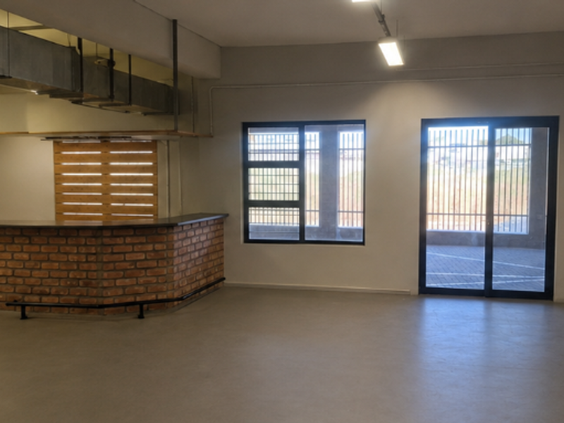 Spacious open-plan office area featuring polished concrete floors, exposed industrial ductwork, and a built-in brick service counter with direct access to the exterior.
