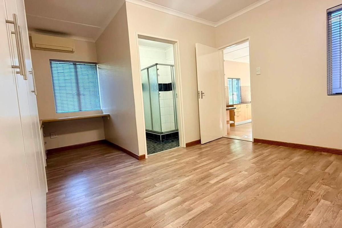 Spacious bedroom featuring laminate flooring, built-in cupboards, an air conditioning unit, and an en-suite bathroom with a shower.