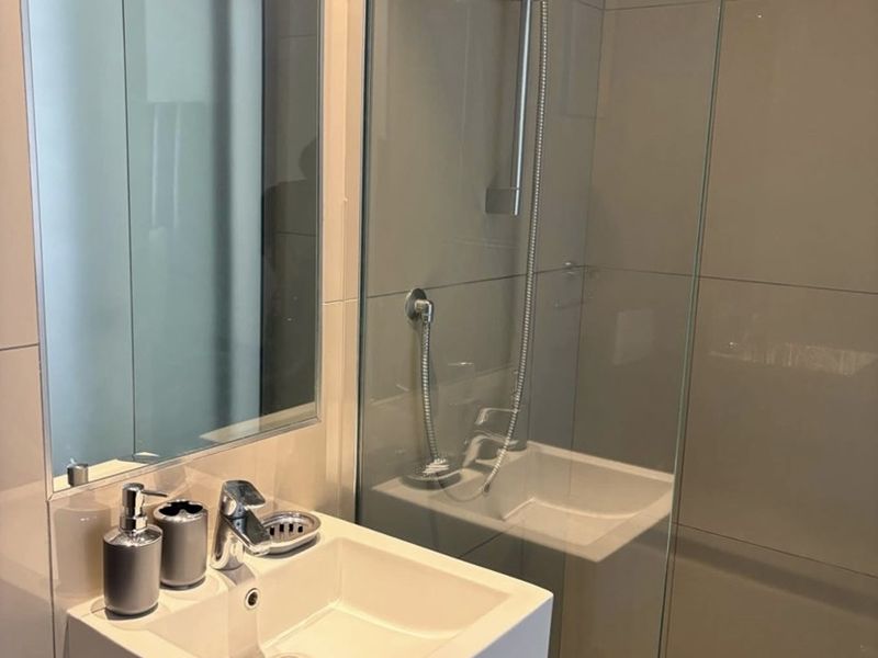 Modern bathroom featuring a wall-mounted basin, chrome fixtures, glass shower enclosure, and neutral large-format wall tiles with mosaic floor detailing.